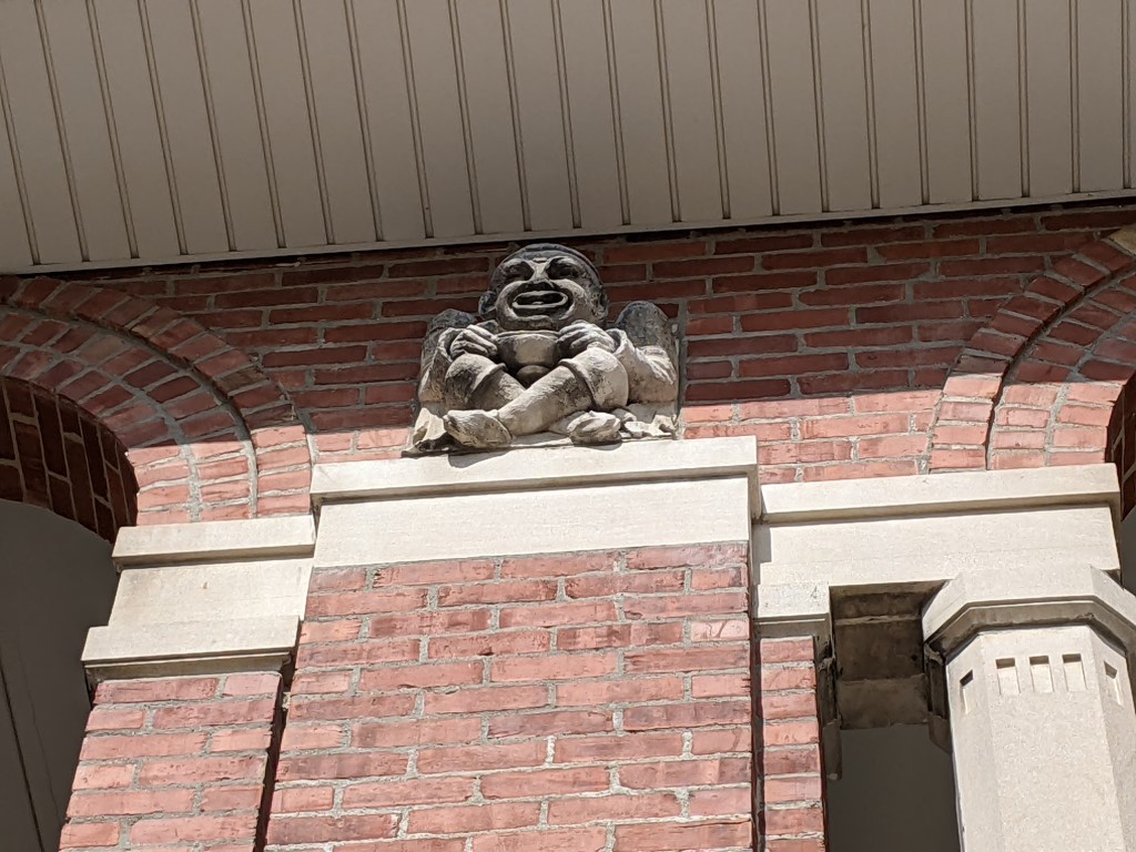 a close up shot of a brown brick building with a cement gargoyle sitting atop a column