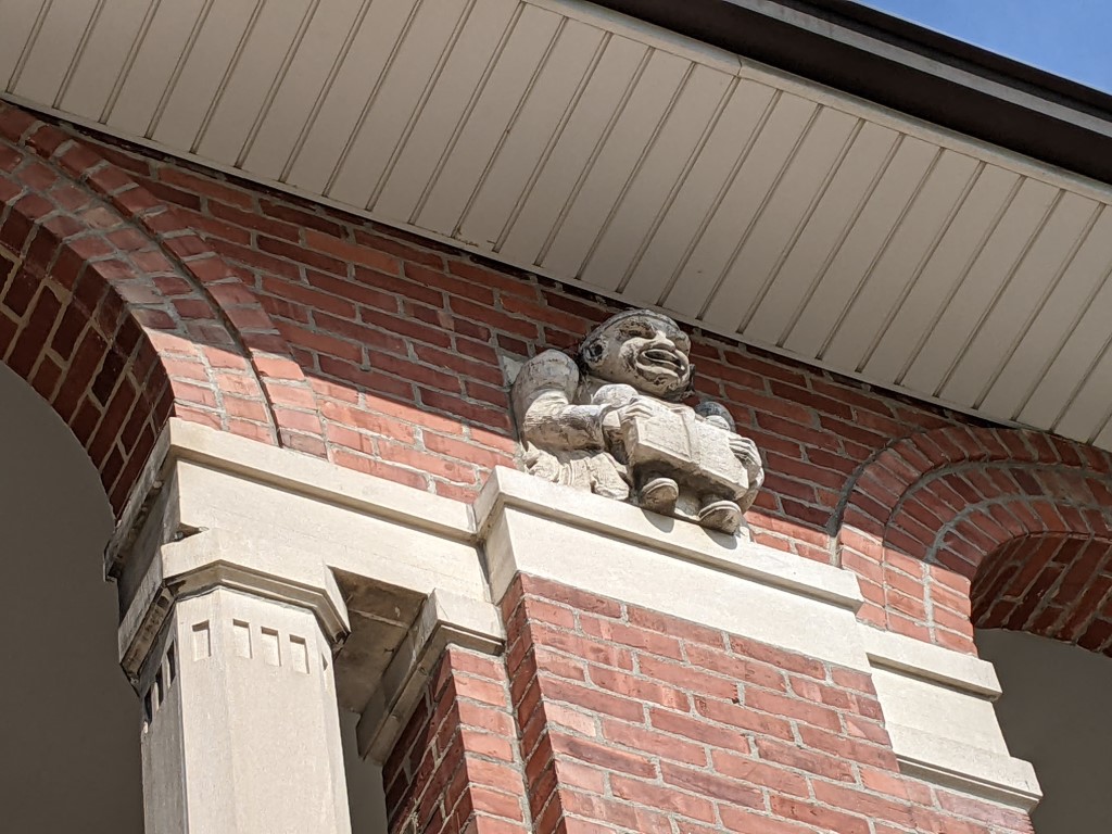 a close up shot of a brown brick building with a cement gargoyle sitting atop a column