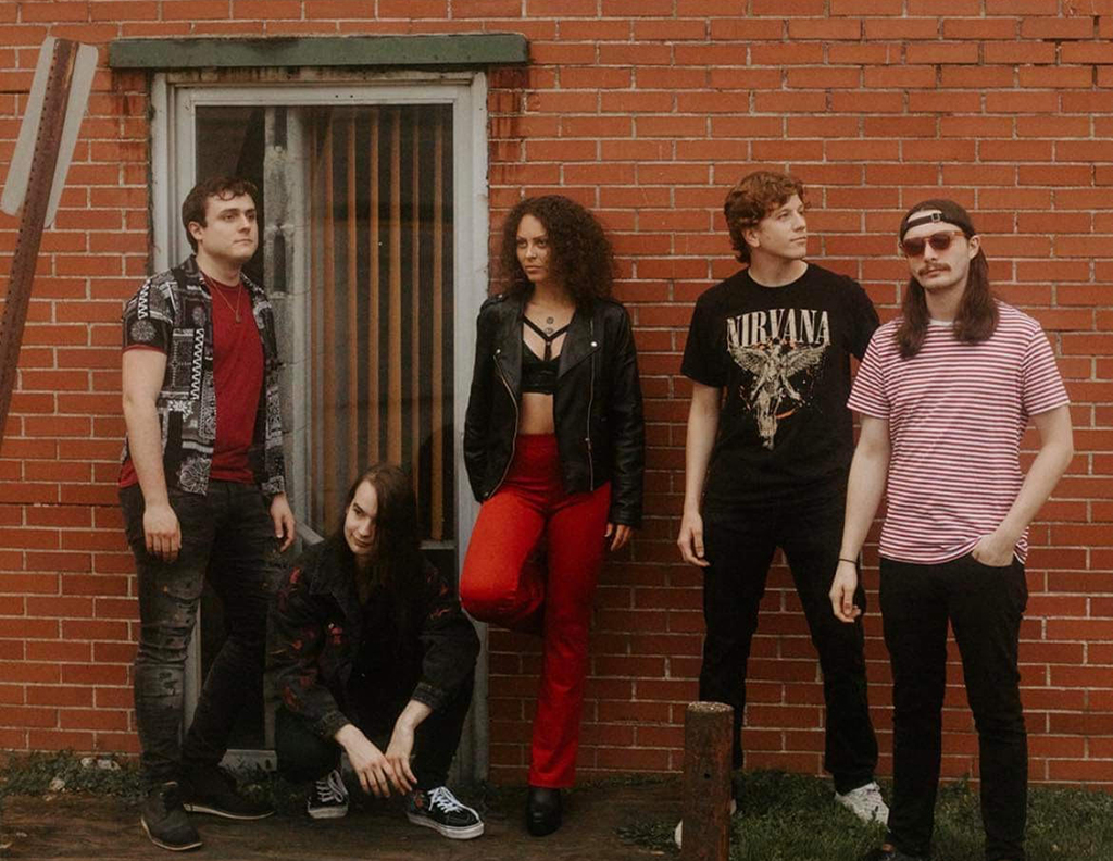 The five members of The Hangovers posing outside against the wall of a brick building. The member on the right looks at the camera, but every other member is looking in a different direction.