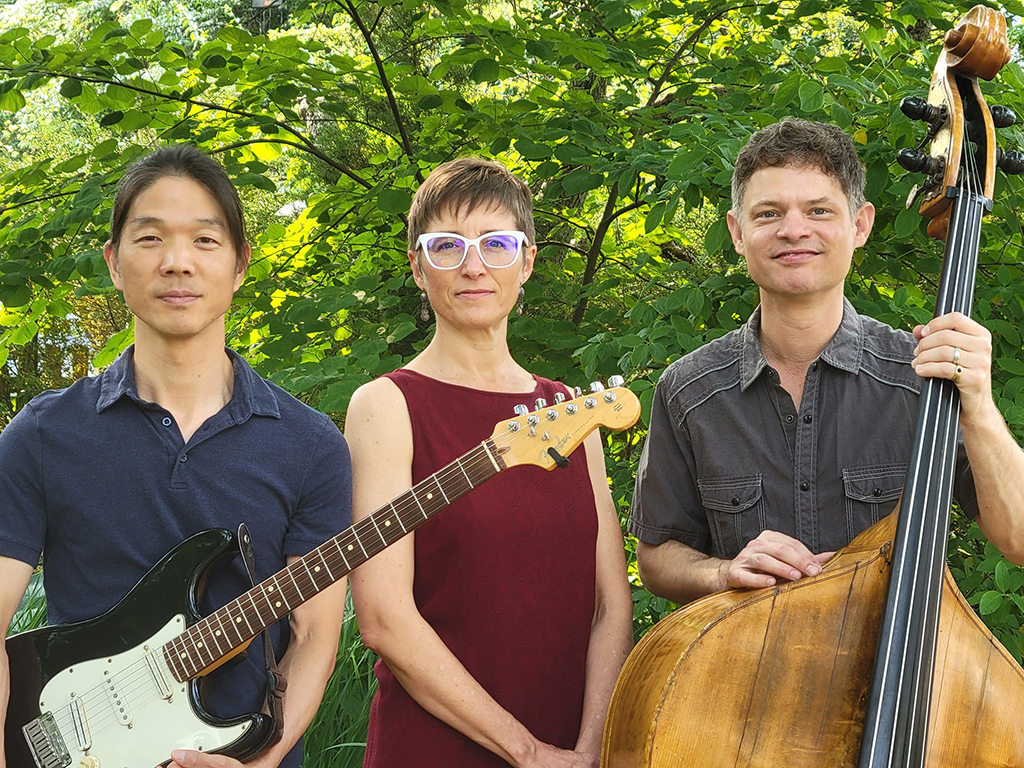 Guitarist, singer and upright bass player posing outdoors in front of some trees.