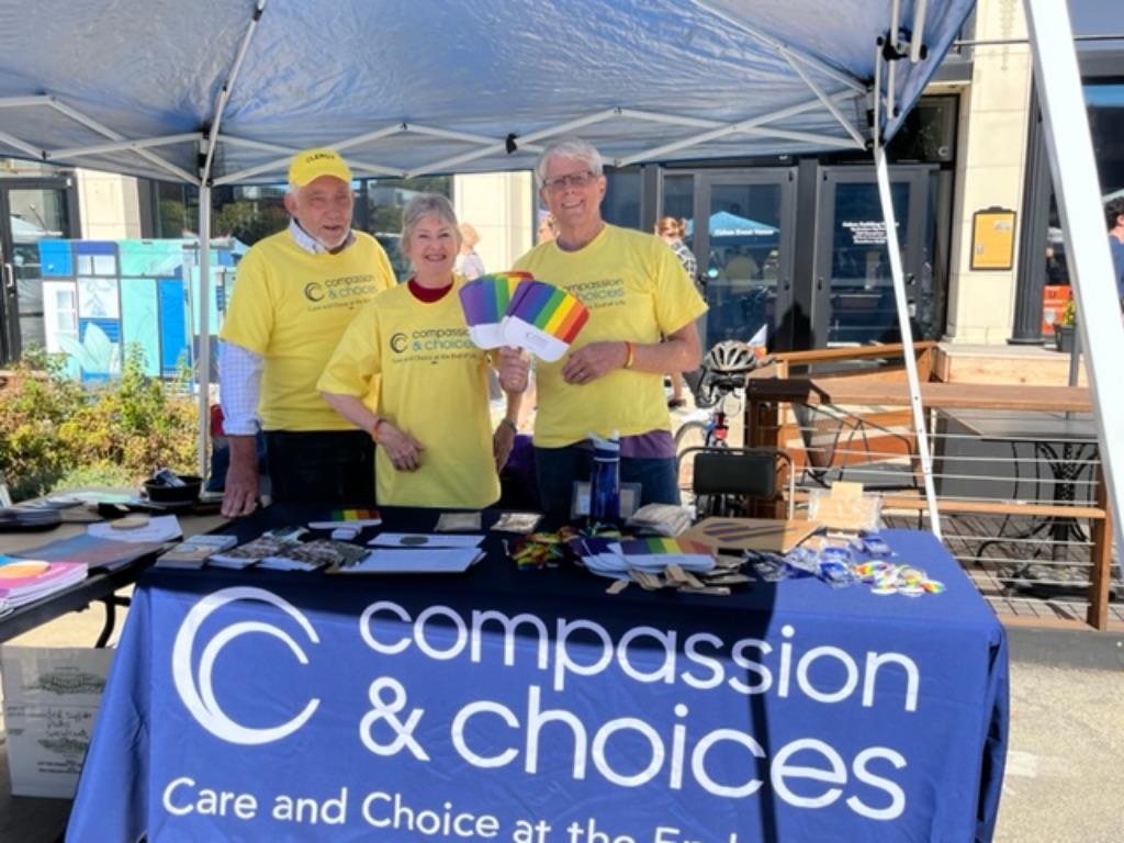 Two white men and a white woman wear yellow shirts and stand behind a blue banner that reads "compassion and choices" .