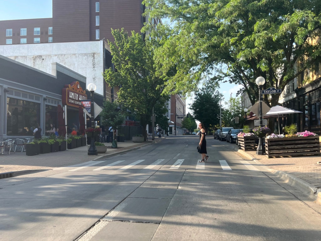 On Neil Street in Downtown Champaign, Katie Carrillo crosses the street in a black dress and espadrille sandals. Photo by Alyssa Buckley.