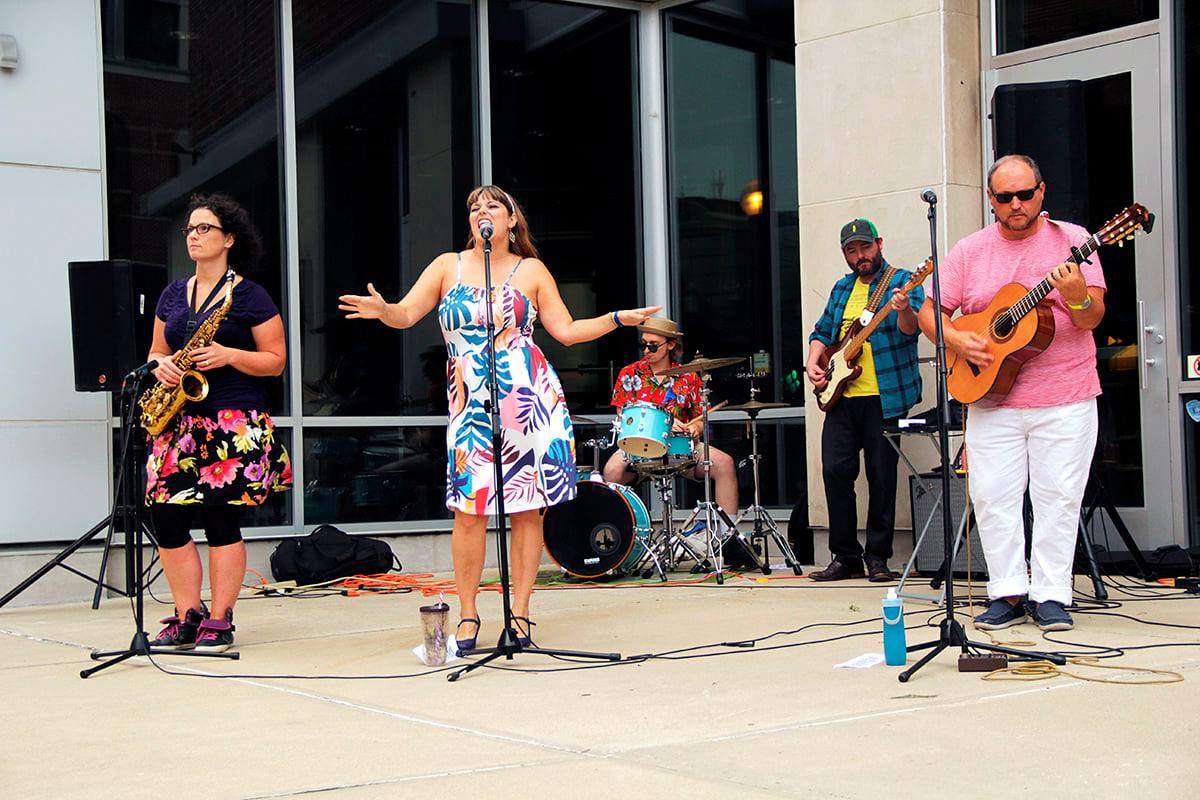 Two women and three men are in a band, performing on a sidewalk.