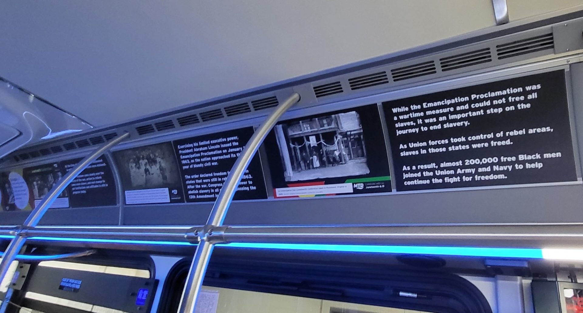 Panels on the interior of a bus that have information about Juneteenth. They have a black background and white text, with a black and white photo.
