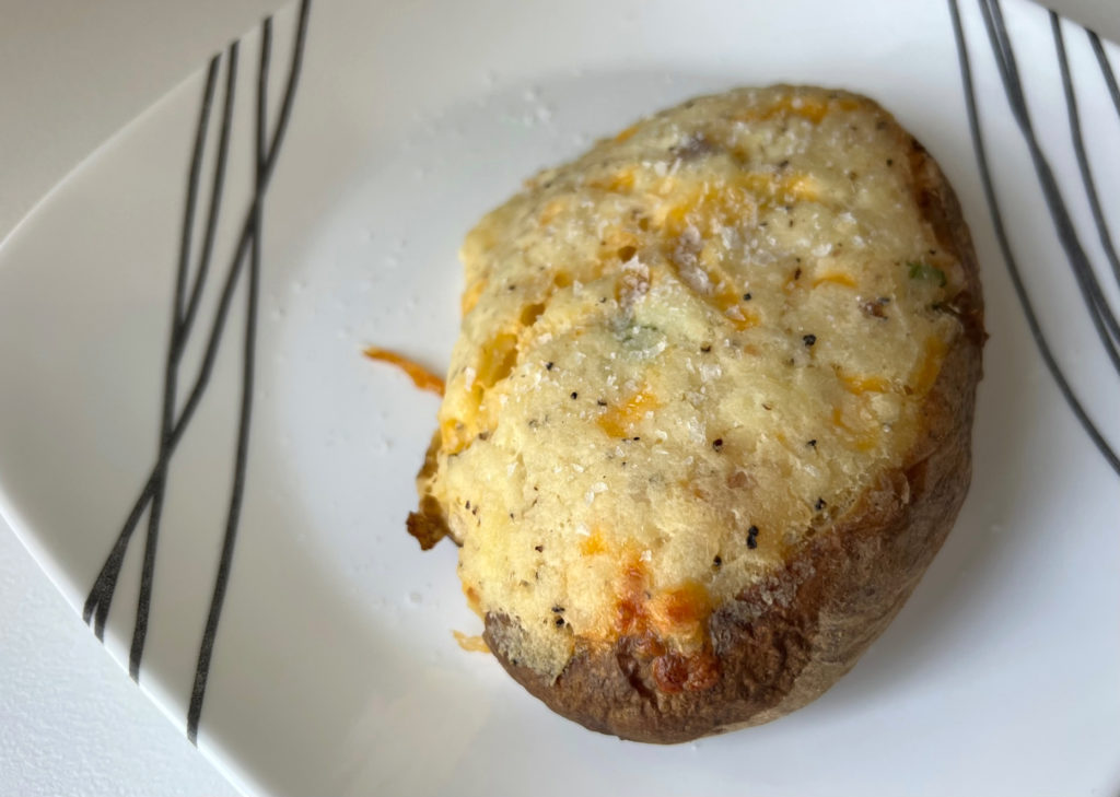 A twice baked potato flecked with pepper and salt, and the cheese is a dark orange from baking in the oven. Photo by Alyssa Buckley.