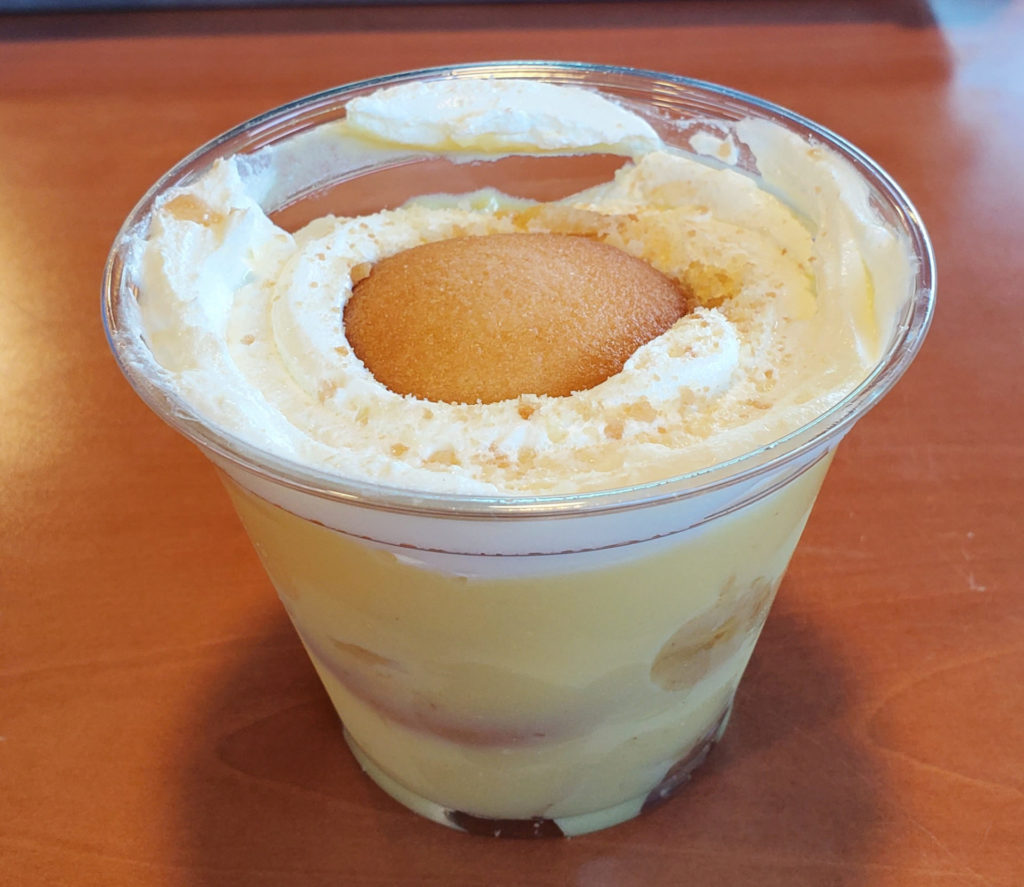 A plastic cup has banana pudding with whipped cream topped with a vanilla wafer cookie. Photo by Carl Busch.