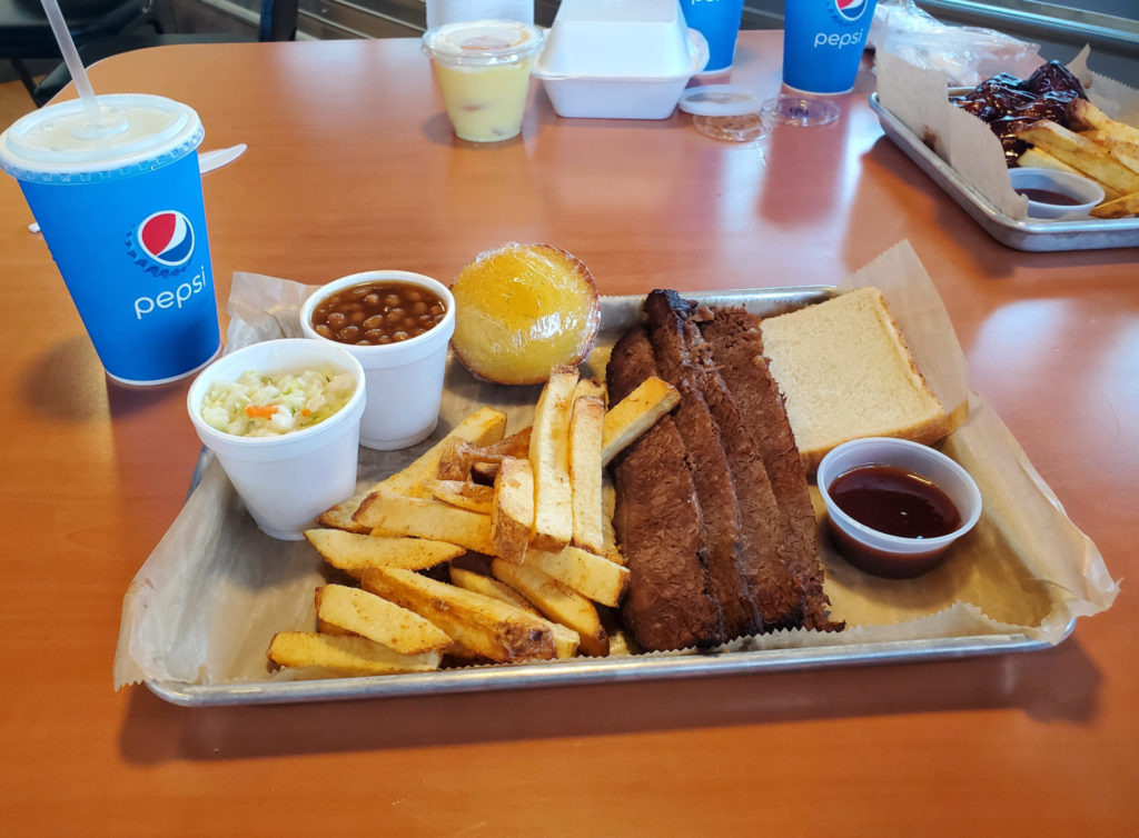 A platter of brisket with a side of sauce, fries, toast, beans, coleslaw, and cornbread muffin are on a table for dine in at Sooie Bros Bar-B-Que Joint. Photo by Carl Busch.