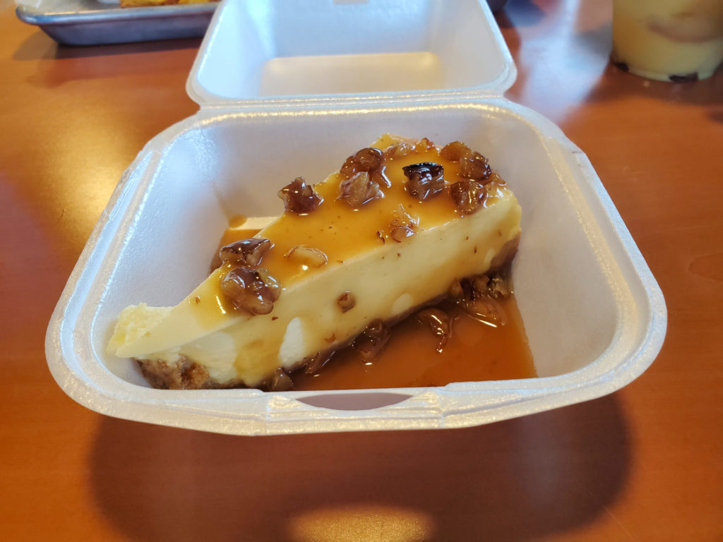 A pecan bourbon cheesecake has a caramel sauce with chopped pecans inside a white styrofoam container. Photo by Carl Busch.