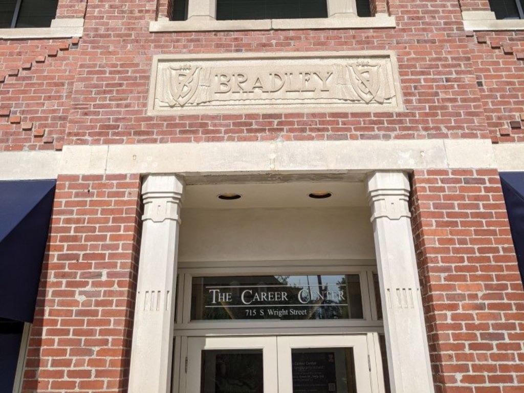 The front door of a brown brick building. Each there is a column on either side of the door. And the worlds "Bradley" are stamped in cement on a plaque above the door. 