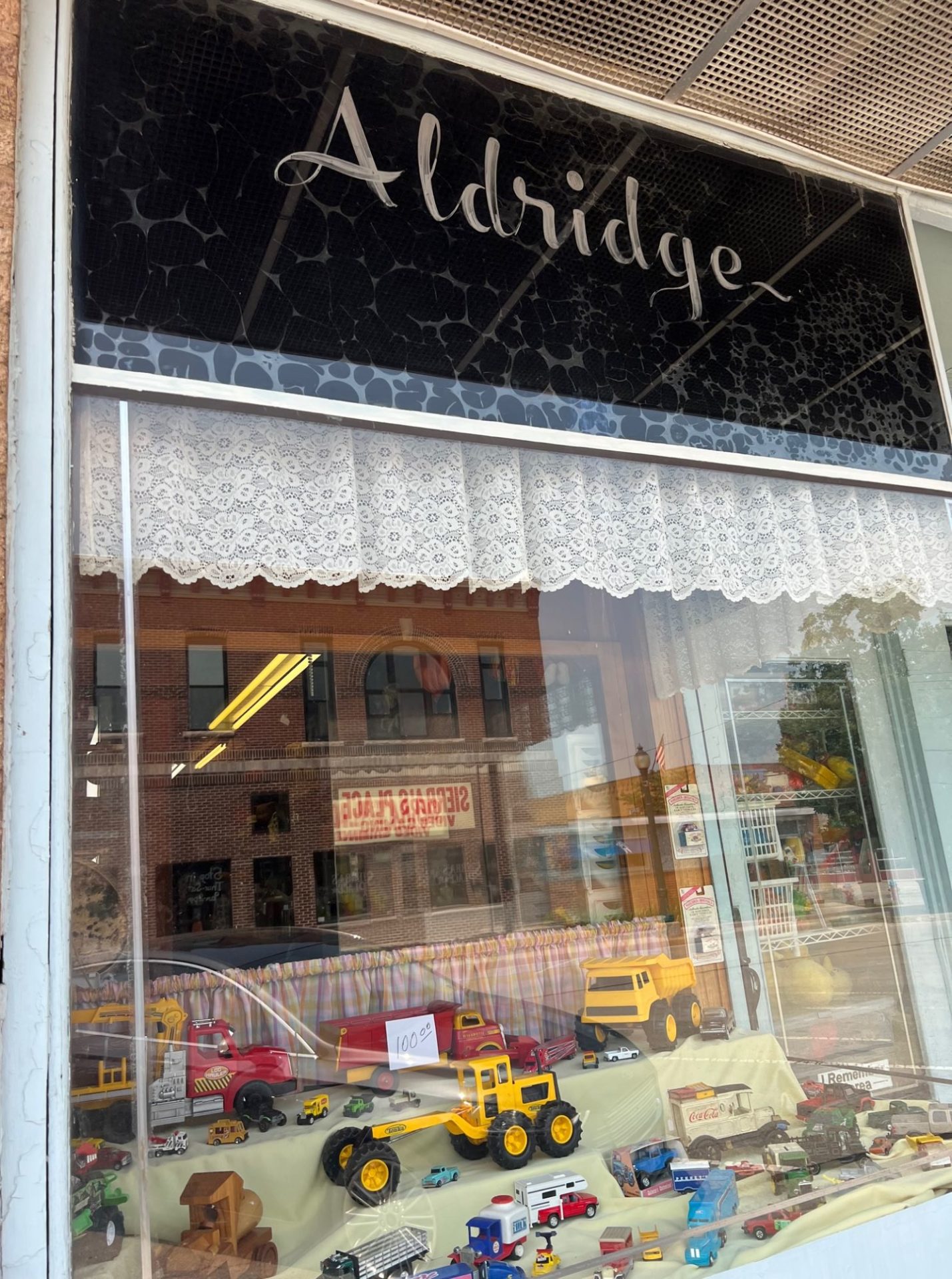 A store window with a display filled with toy trucks of all sizes. Above the window is a black sign with the word Aldridge in white script.