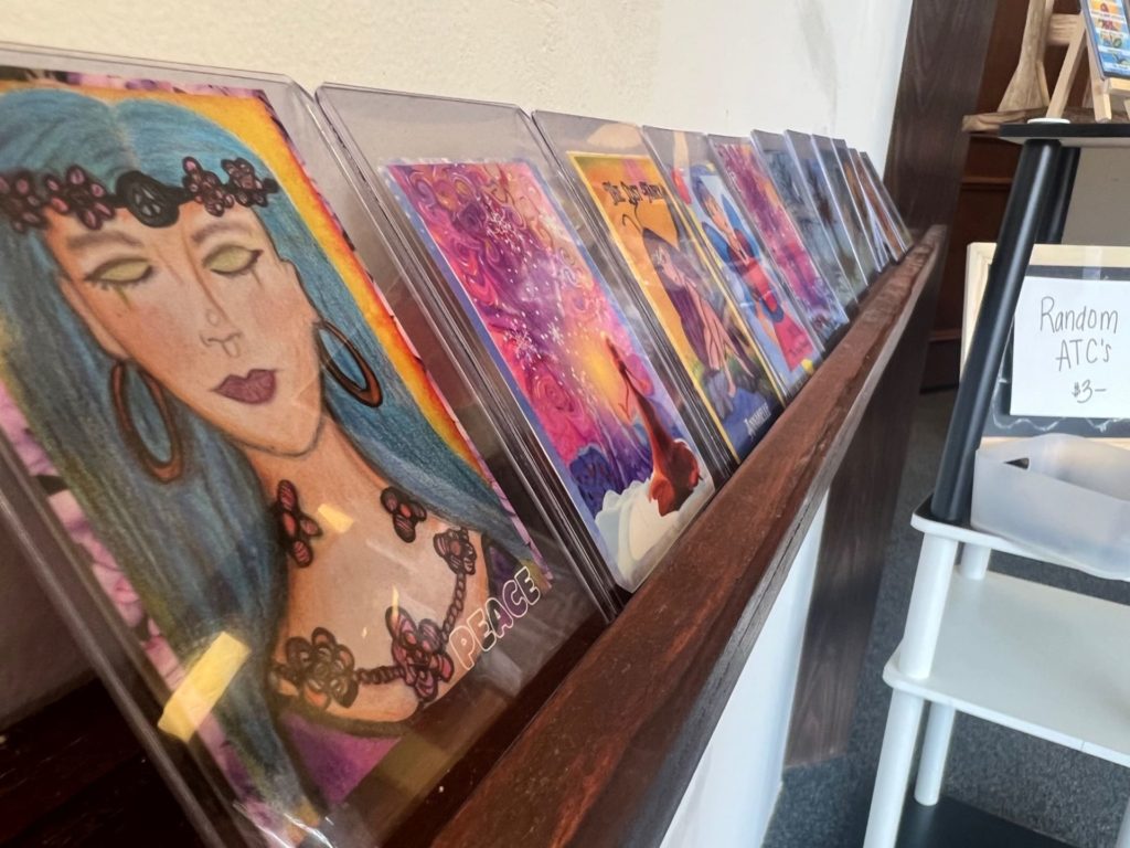 A wooden shelf line with colorful trading card sized pieces of artwork.