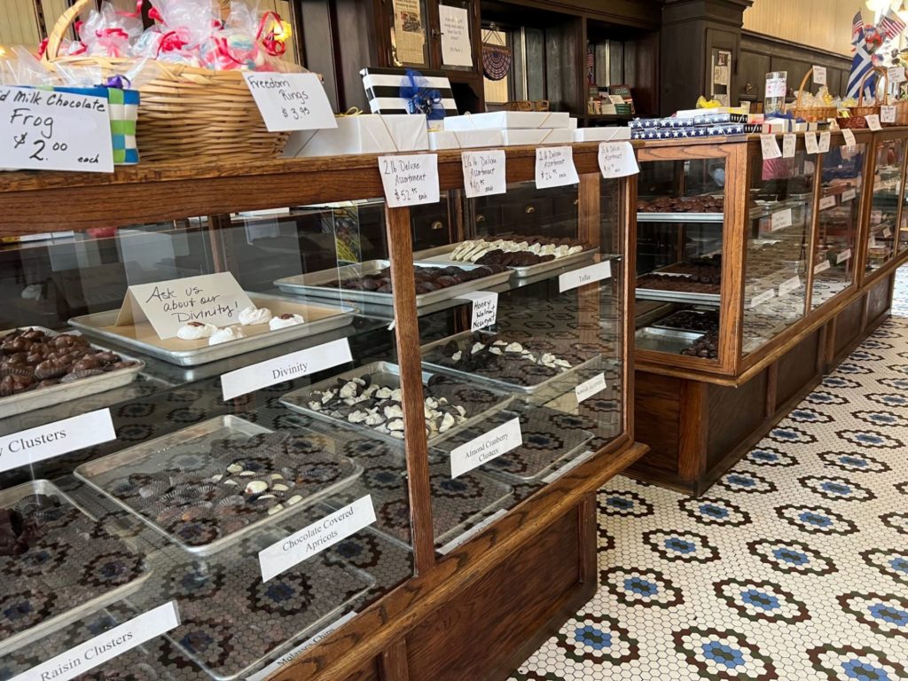 Two large display cases with trays of chocolates inside. There are packaged candies sitting along the top. The floor is white, blue, and brown mosaic tiles.
