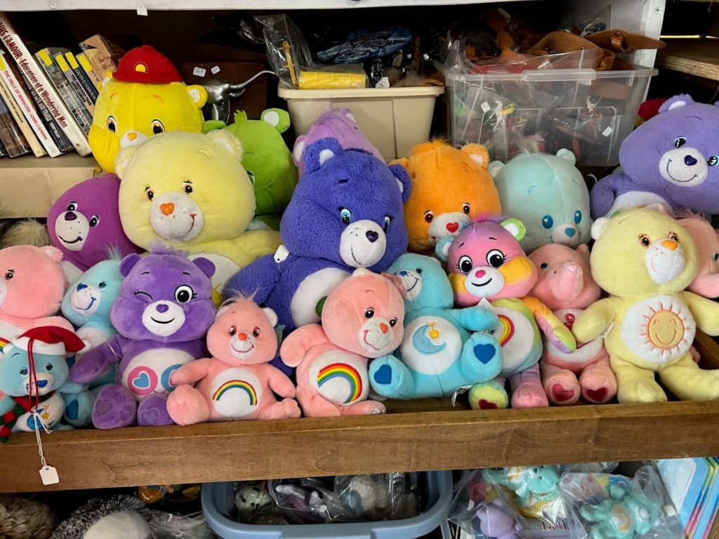 A wooden shelf that is stuffed full with different sizes and colors of Care Bears.