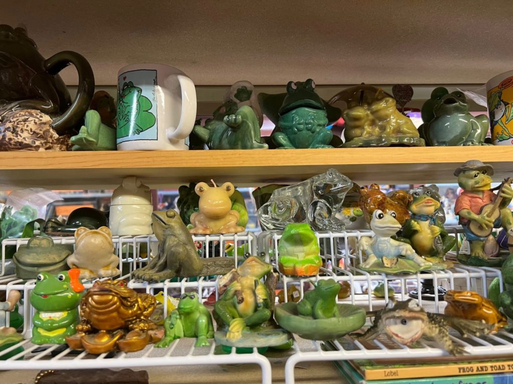White metal and light wood shelving lined with ceramic frog figurines. 