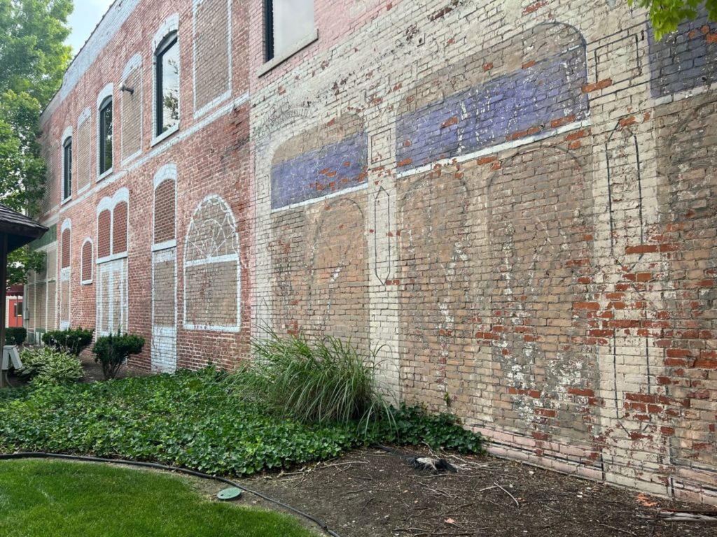 A brick facade of a building that has faded images of windows painted on it.