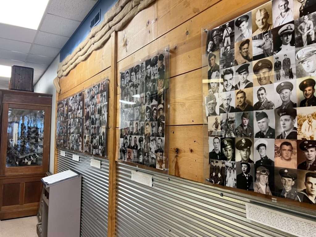 A wood planked wall with metal below. There are several photo collages of square photos of people in military uniforms.