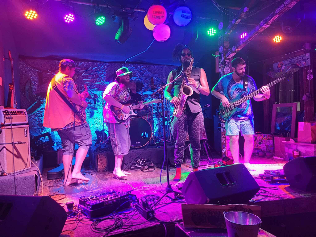 This is a photo of a band performing on a stage in a nightclub. The stage is decorated with colorful lanterns and lights. The band members are playing various instruments, including guitars, saxophone, and drums. There are speakers and other musical equipment on the stage.