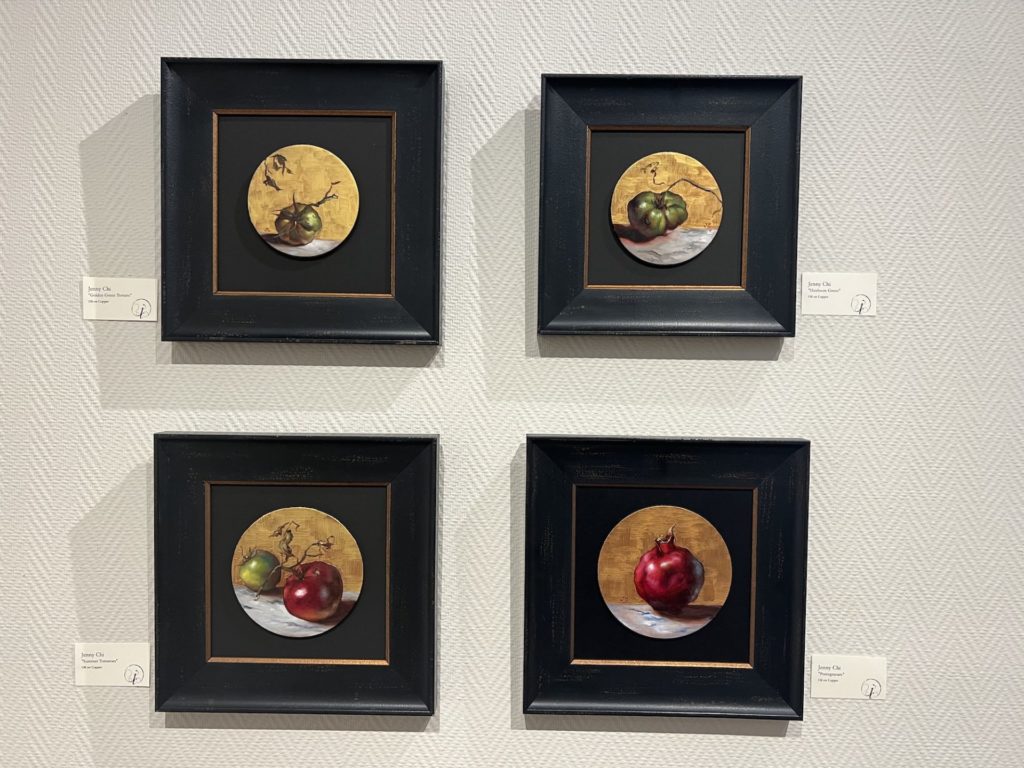 a collection of four oil on copper paintings. Each copper is round and displayed on a square black frame. Each features a still life of a piece of fruit. 