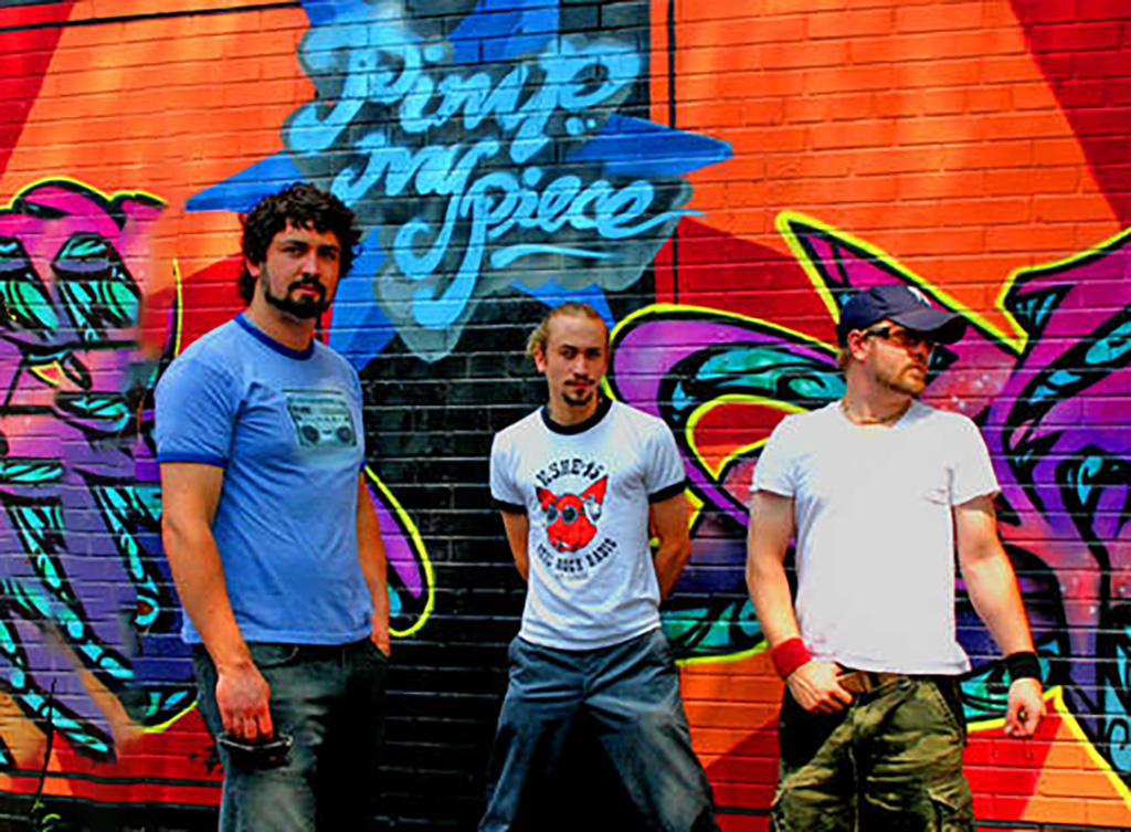 3 members of Lorenzo Goetz standing in front of a wall with bright neon graffiti.
