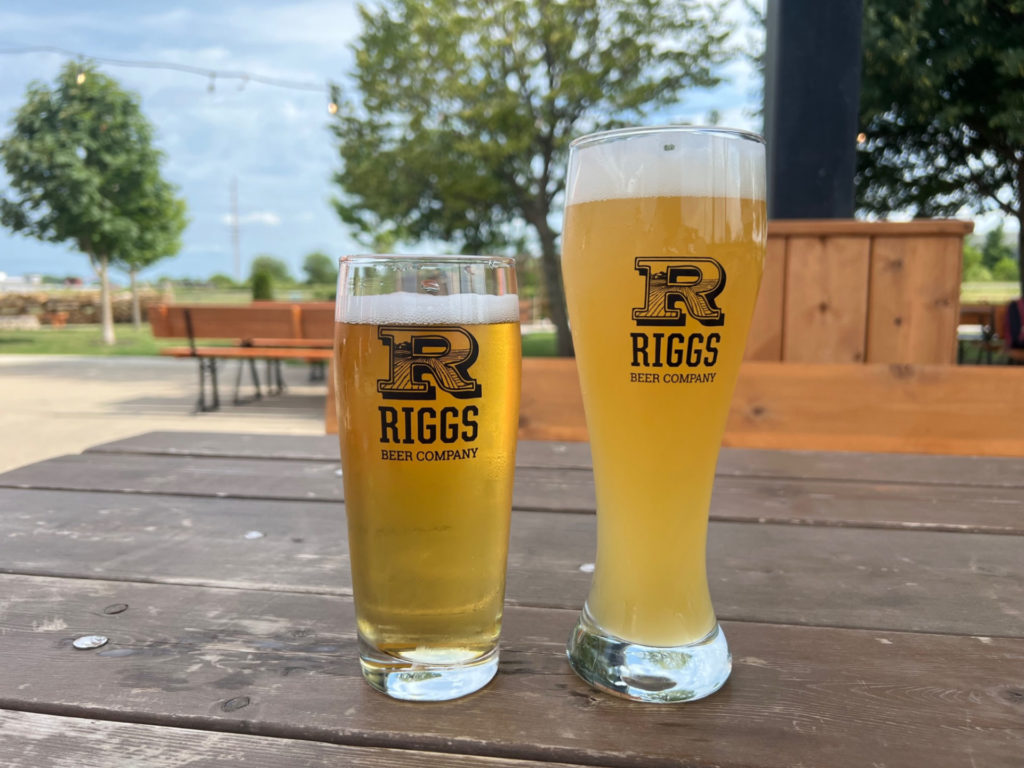 Two beers from Riggs Beer Company sit on a weathered brown table at Riggs' beer garden in Urbana. Photo by Alyssa Buckley.