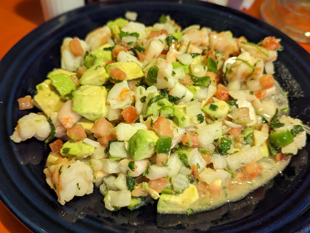 A close-up of fresh shrimp, avocado chunks, diced tomatoes & onions plated on a dark blue plate. Photo by Tayler Neumann.