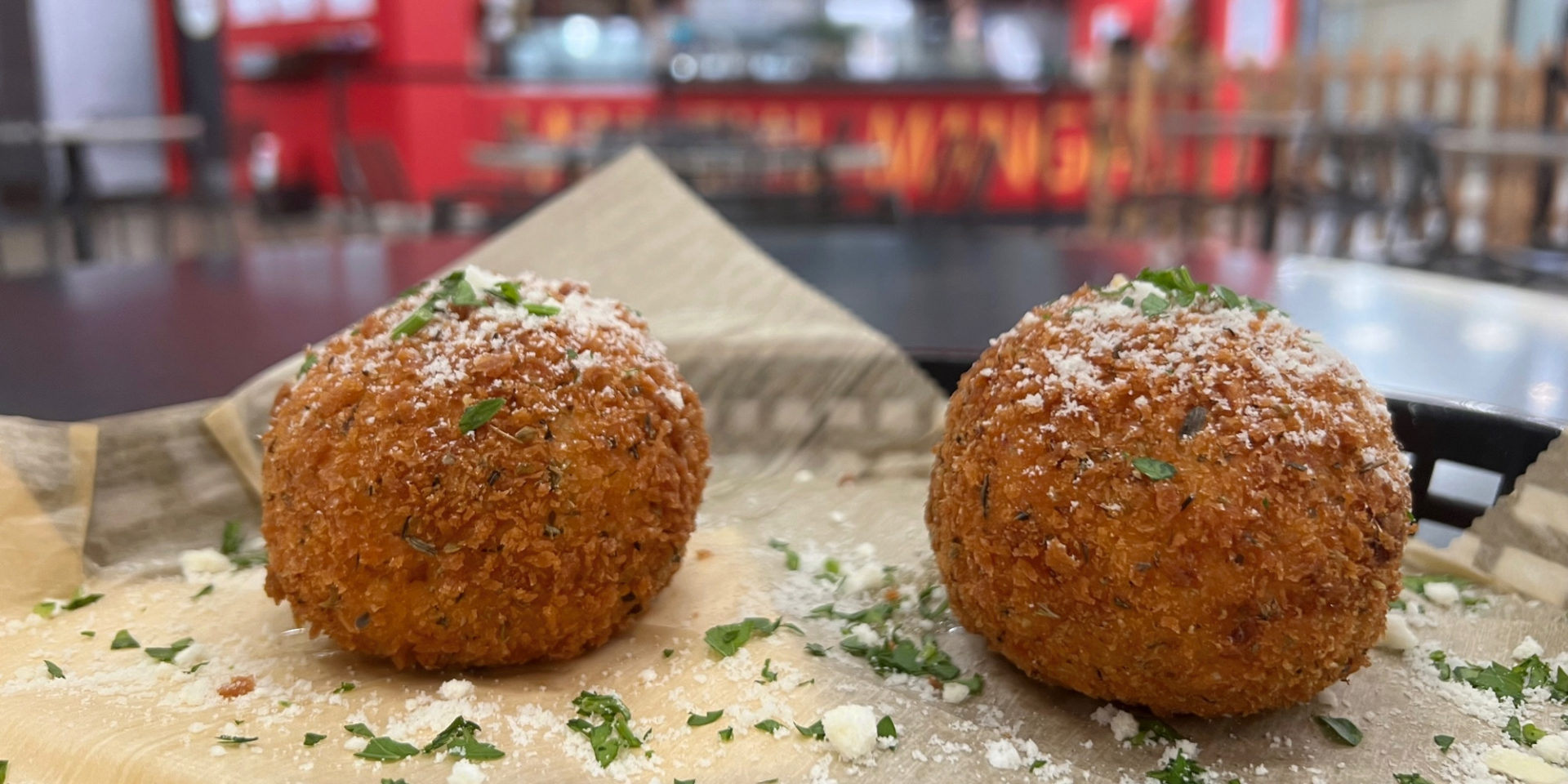 Baldarotta's arancini in a cropped image of two aranici dusted with Parmesan in a black plastic basket at Baldarotta's in the Lincoln Square Mall. Photo by Alyssa Buckley.