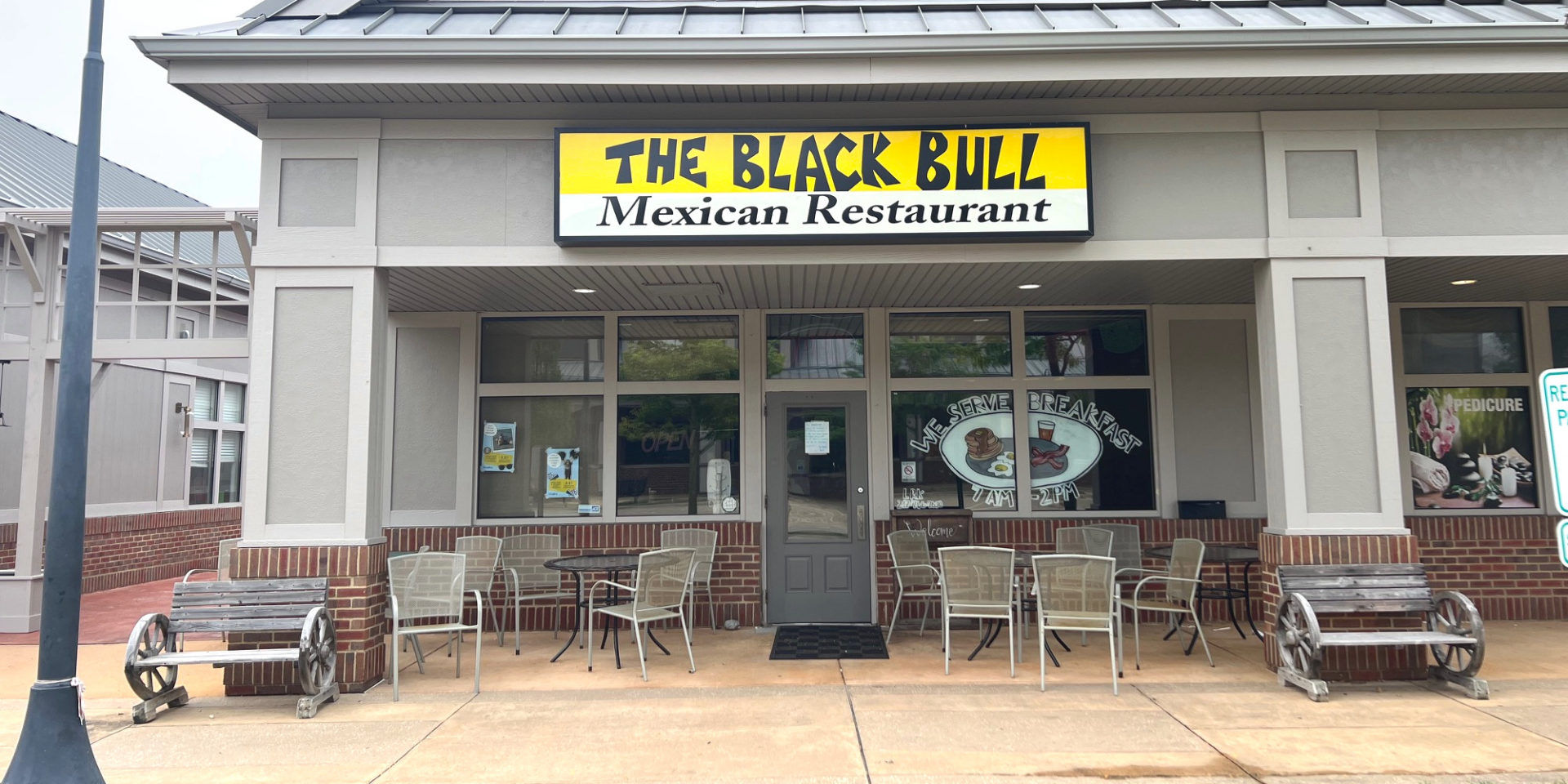 The exterior of The Black Bull restaurant has a yellow sign above patio furniture in The Crossing plaza of Champaign, Illinois. Photo by Alyssa Buckley.