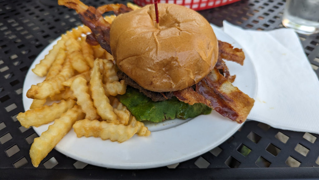 A burger with bacon sticking out the sides and a side of crinkle fries are on a white plate. Photo by Taylor Judd.
