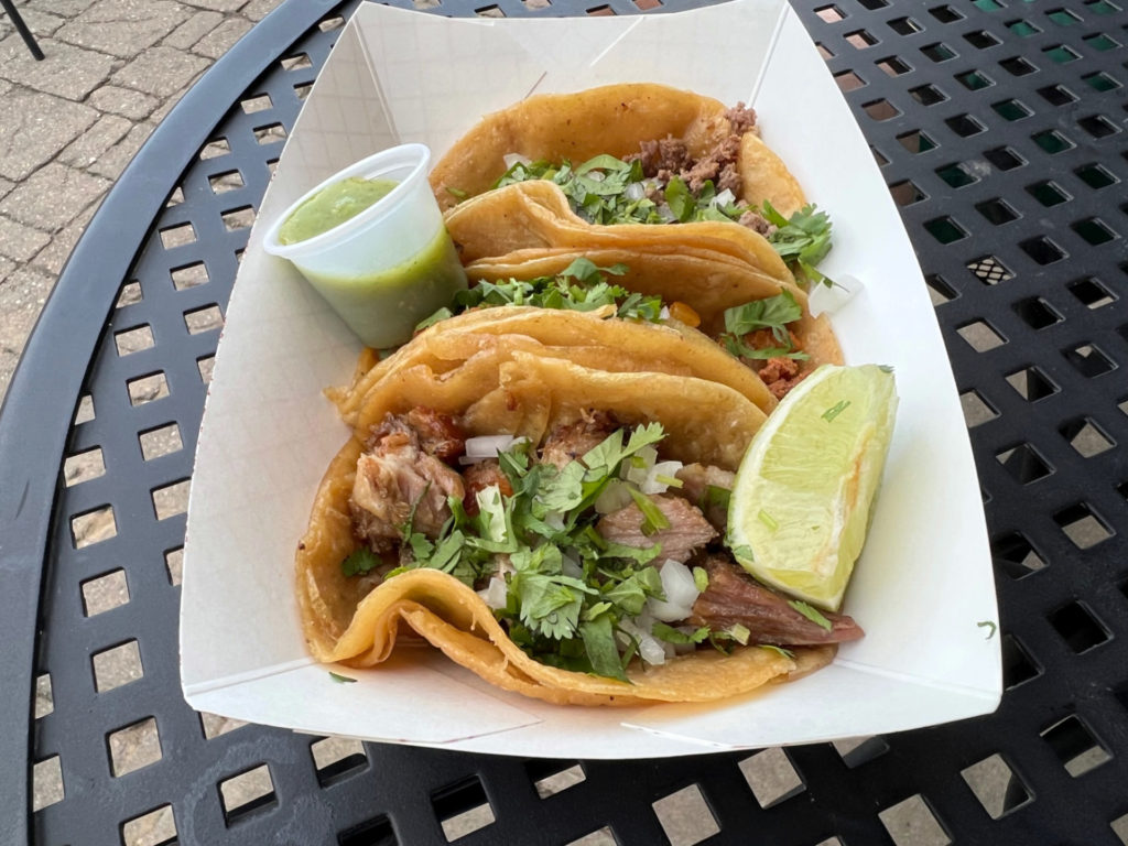 Three tacos from La Paloma food truck in Champaign are in a white basket on a black patio table at Triptych Brewing. Photo by Alyssa Buckley.