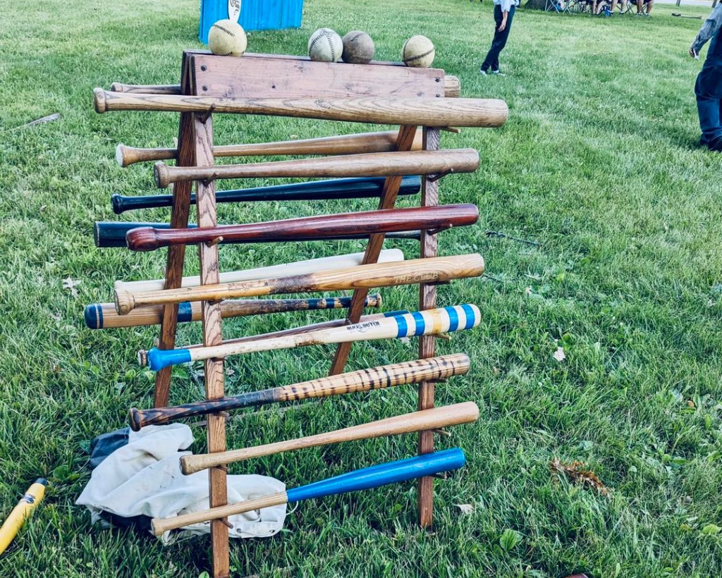 A tower stand holds a variety of vintage base ball bats in a grassy field. 