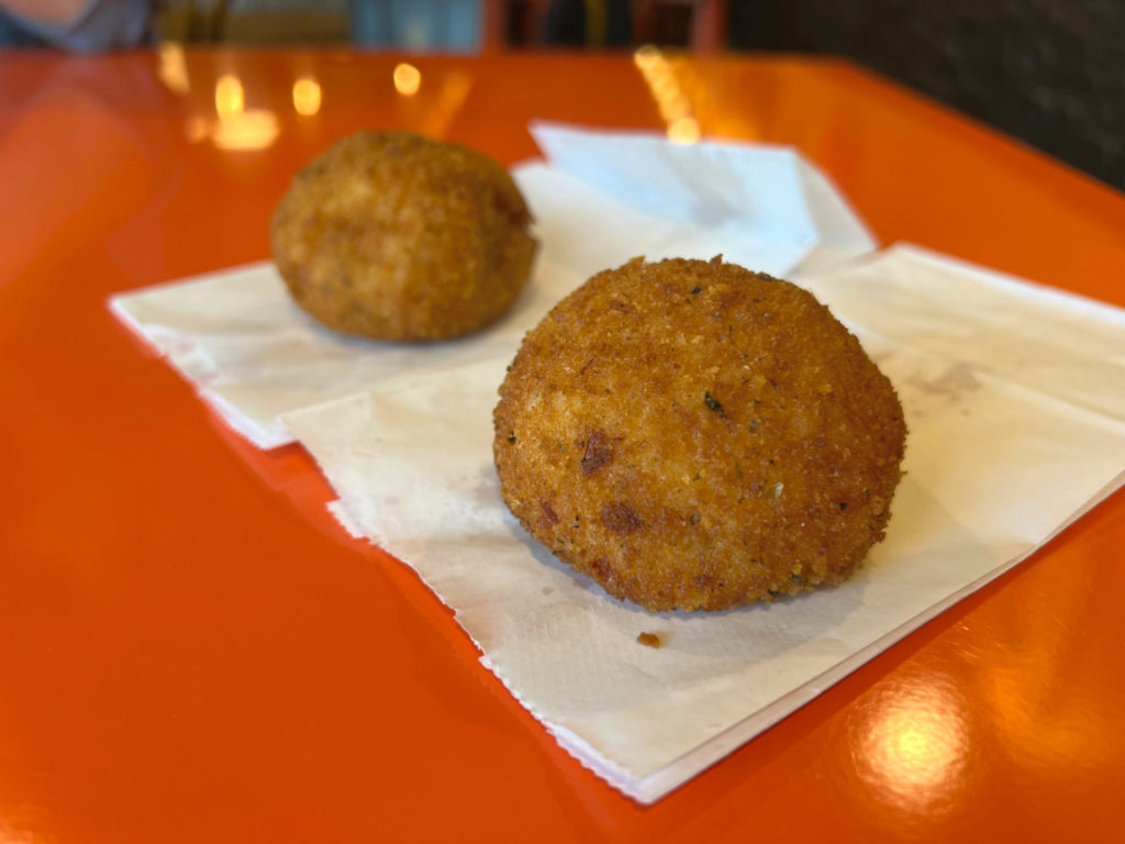 Two big balls of arancini with Italian seasonings sit on white paper bags. Photo by Alyssa Buckley.