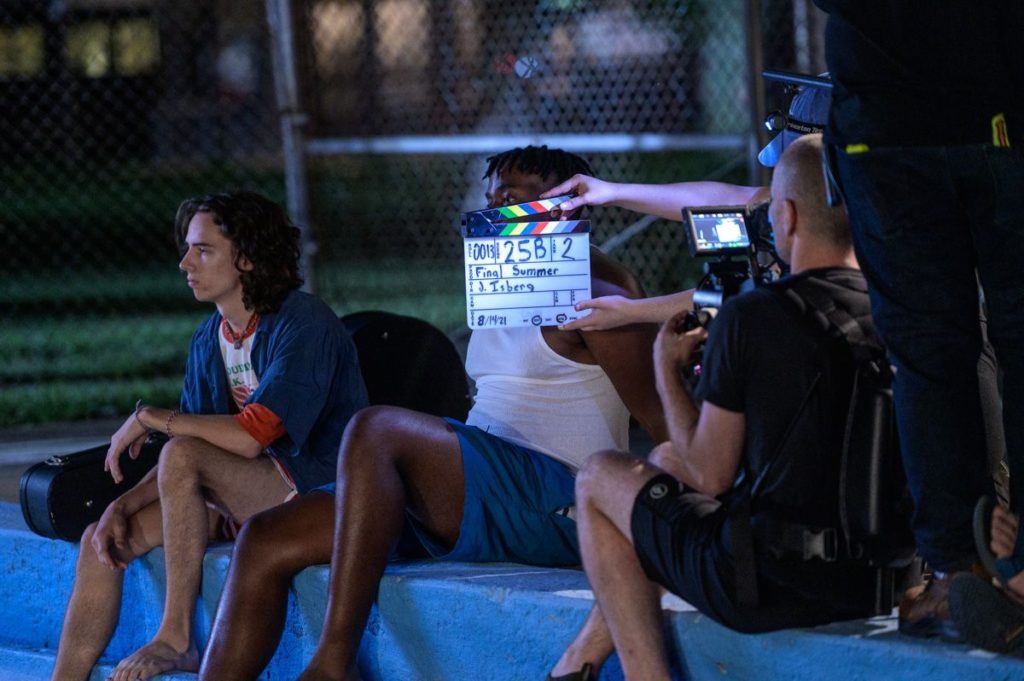 behind the scenes of Final Summer. Actors sit outside at night looking off in the distance; a camera man and director are visible holding up a clapper