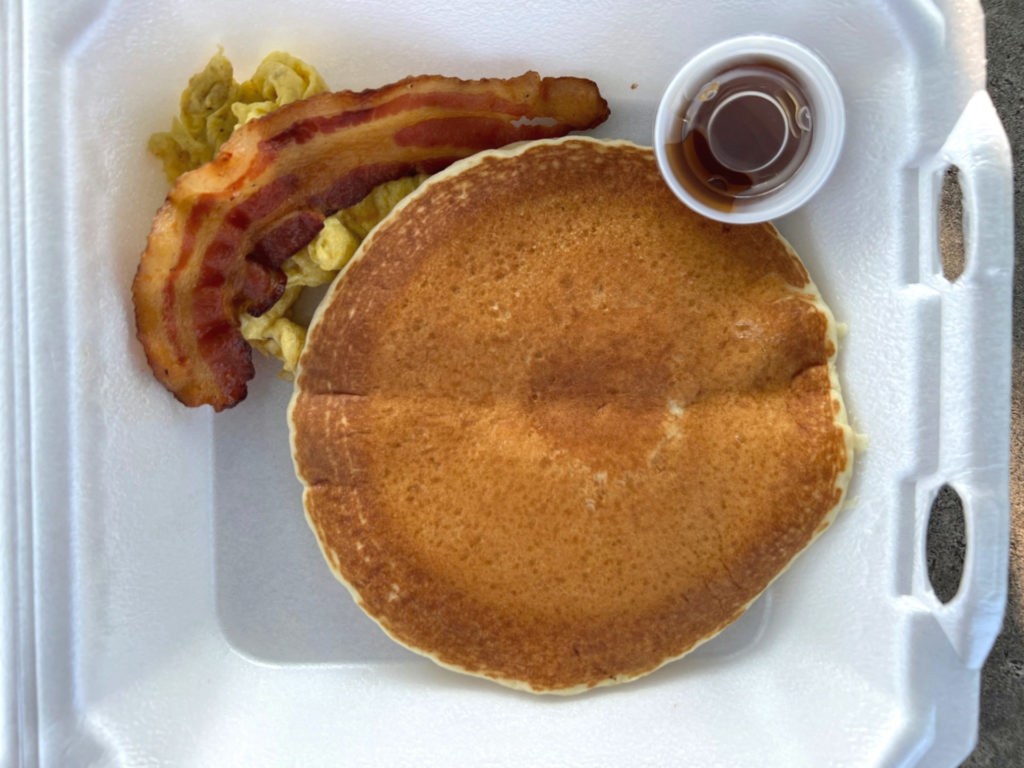 An overhead photo of a pancake with a slice of bacon and eggs with a tiny cup of syrup. Photo by Alyssa Buckley.