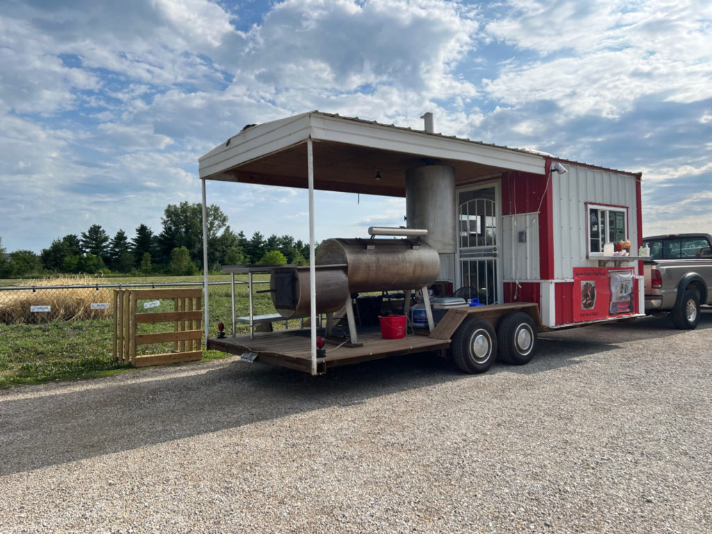 The back view of Mama Duke's food truck which has a metal smoker on the back. The trailer is parked at Riggs on a sunny July day in Urbana, Illinois. Photo by Alyssa Buckley.