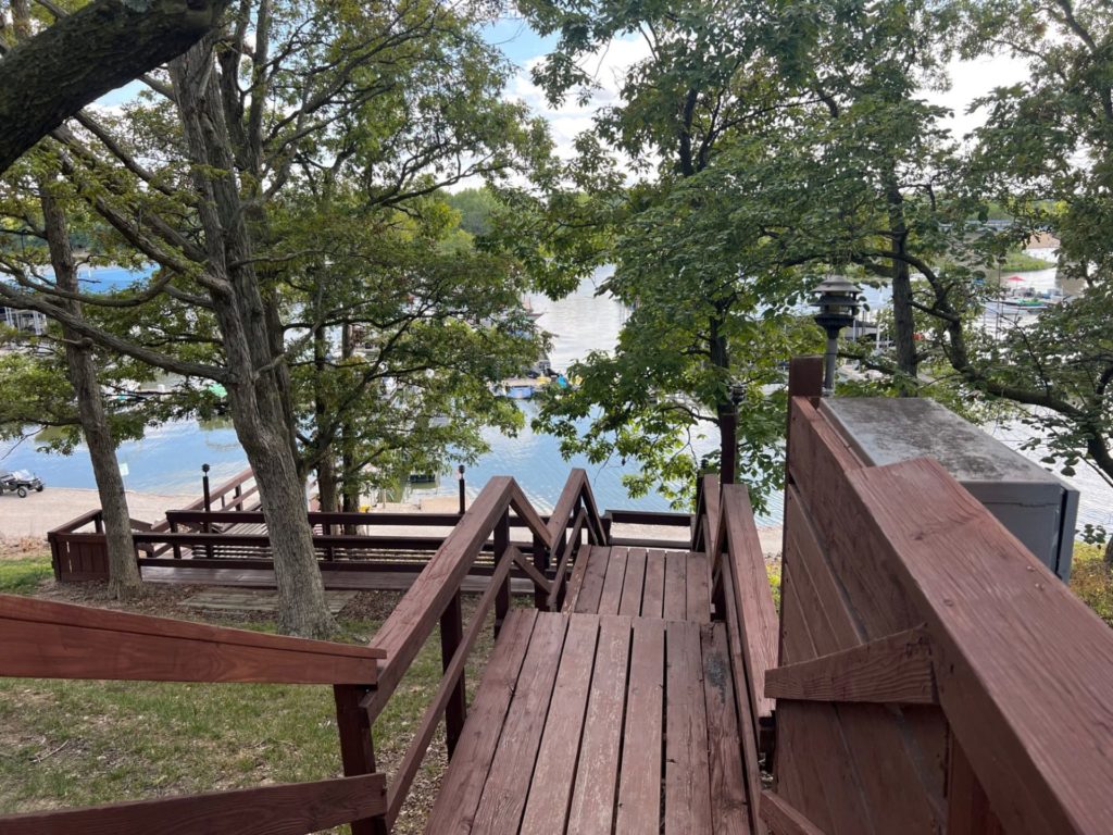 A set of brown wooden stairs leading down to a lake. There are trees alongside the stairs.