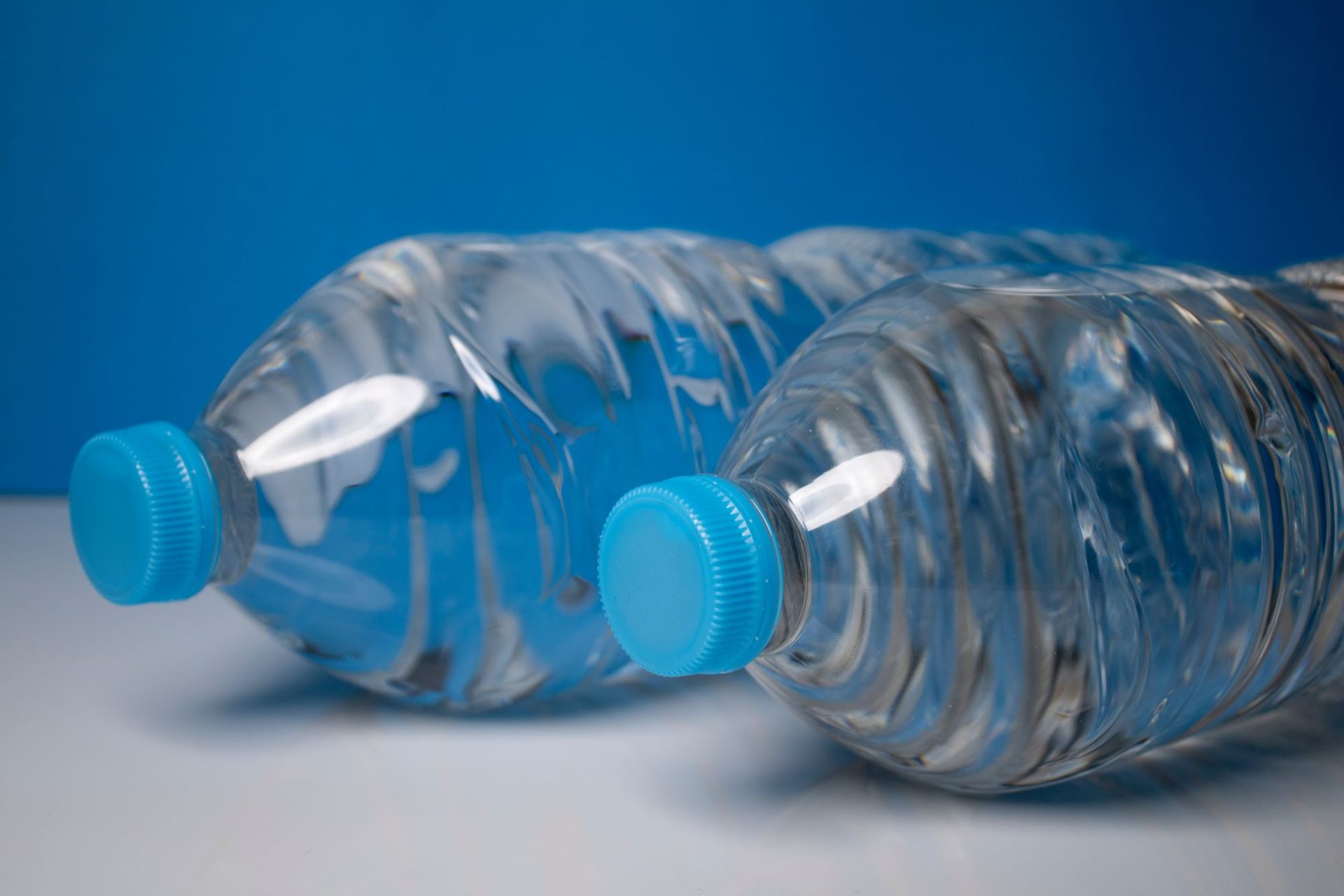 Close up of two plastic water bottles, laying on their sides on a white table.