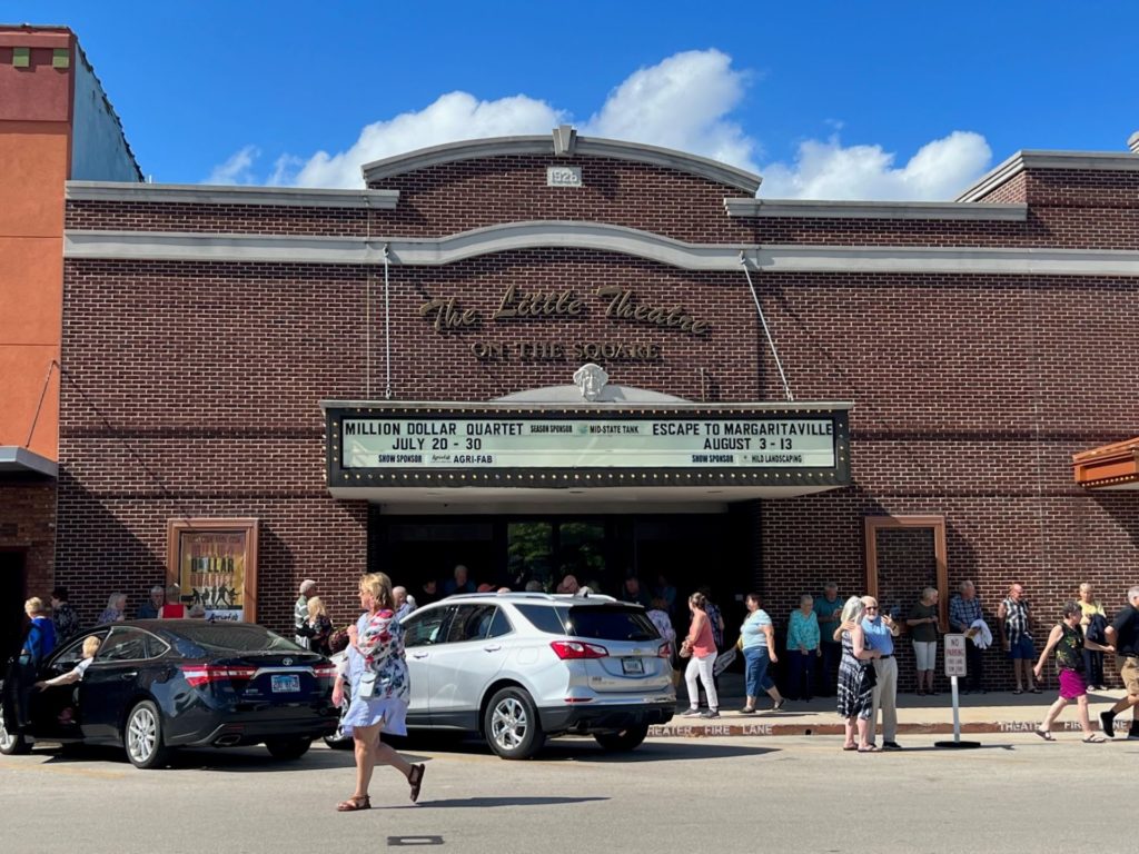 A brown brick building facade with a marquee on the front. Above the marquee is script that says The Little Theatre and block letters that say On The Square.