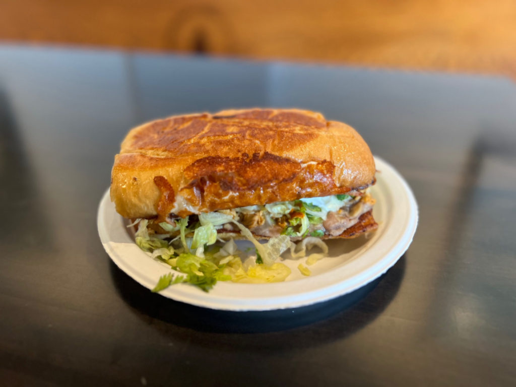 A chicken torta from La Paloma food truck is on a white paper plate on a black table. Photo by Alyssa Buckley.