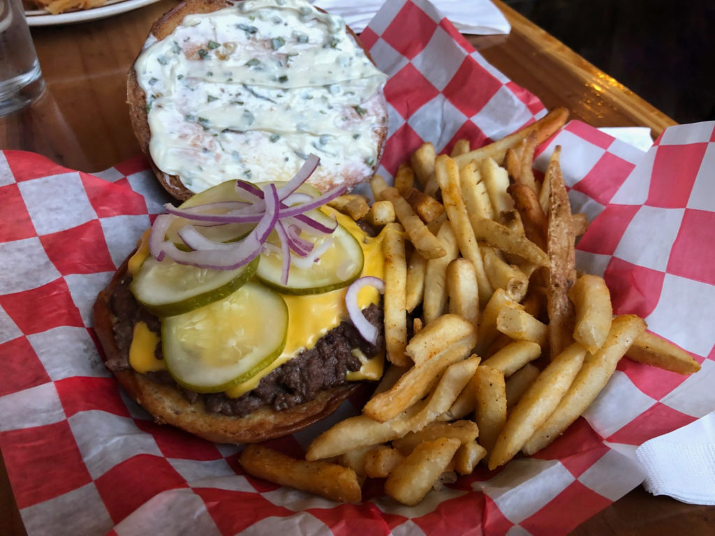The smashburger at Watson's is served open with a garlic herb mayo spread on the top bun, and the bottom bun has meat with three pickles, raw red onions, and a side of seasoned fries. Photo by Alyssa Buckley.