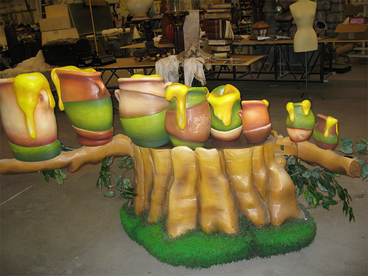 Set design for Disney Playhouse 2, Winnie the Pooh; a large structure in yellow, green, and browns shows honey pots on a tree stump