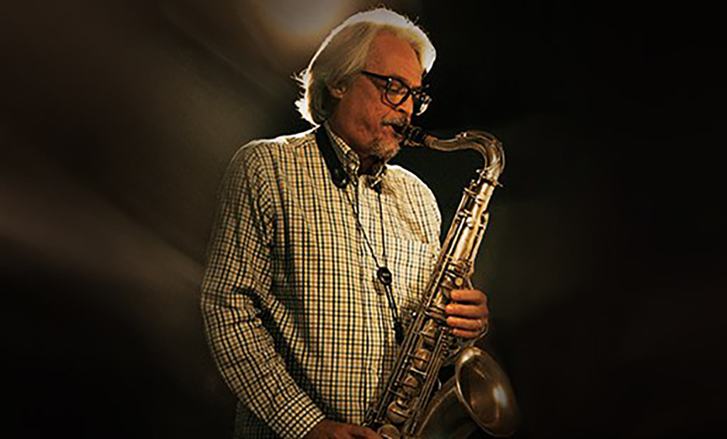 The image is a photo-realistic image of a person playing a saxophone. The person is wearing a checkered shirt and a necklace, and is holding the golden-colored saxophone with both hands. The background is black with a spotlight shining on the person.