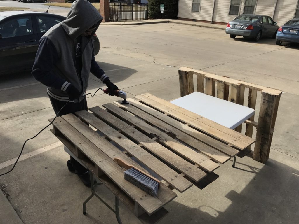 Planks of wood are being prepared by an individual in a gray and black hoodie outside. Photo courtesy of Caribbean Grill.