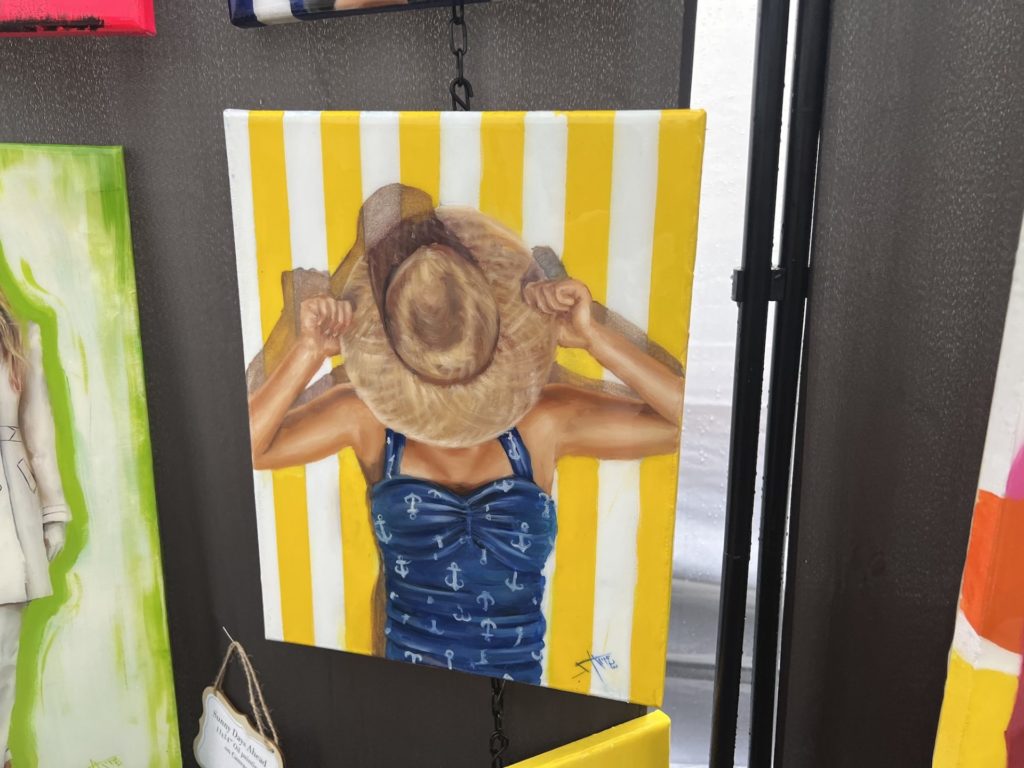  a painting of a woman laying in a blue bathing suit, she is holding a tan hat over her face. the background is white and yellow vertical stripes. 