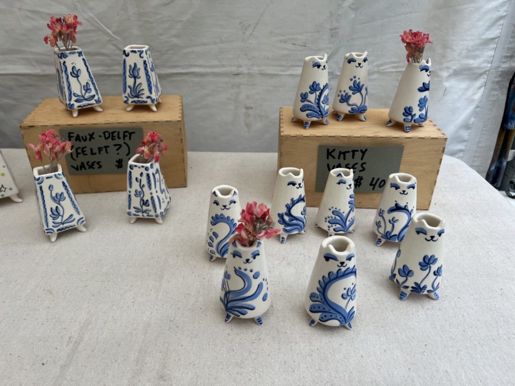 tiny blue and white vases sit on a table; some with an individual pink flower in theme. The vases resemble cats