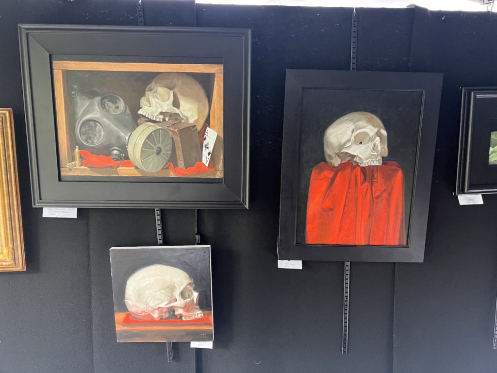 Three paintings by Sara Jahn of skulls with red accents and black backgrounds hang against a black wall