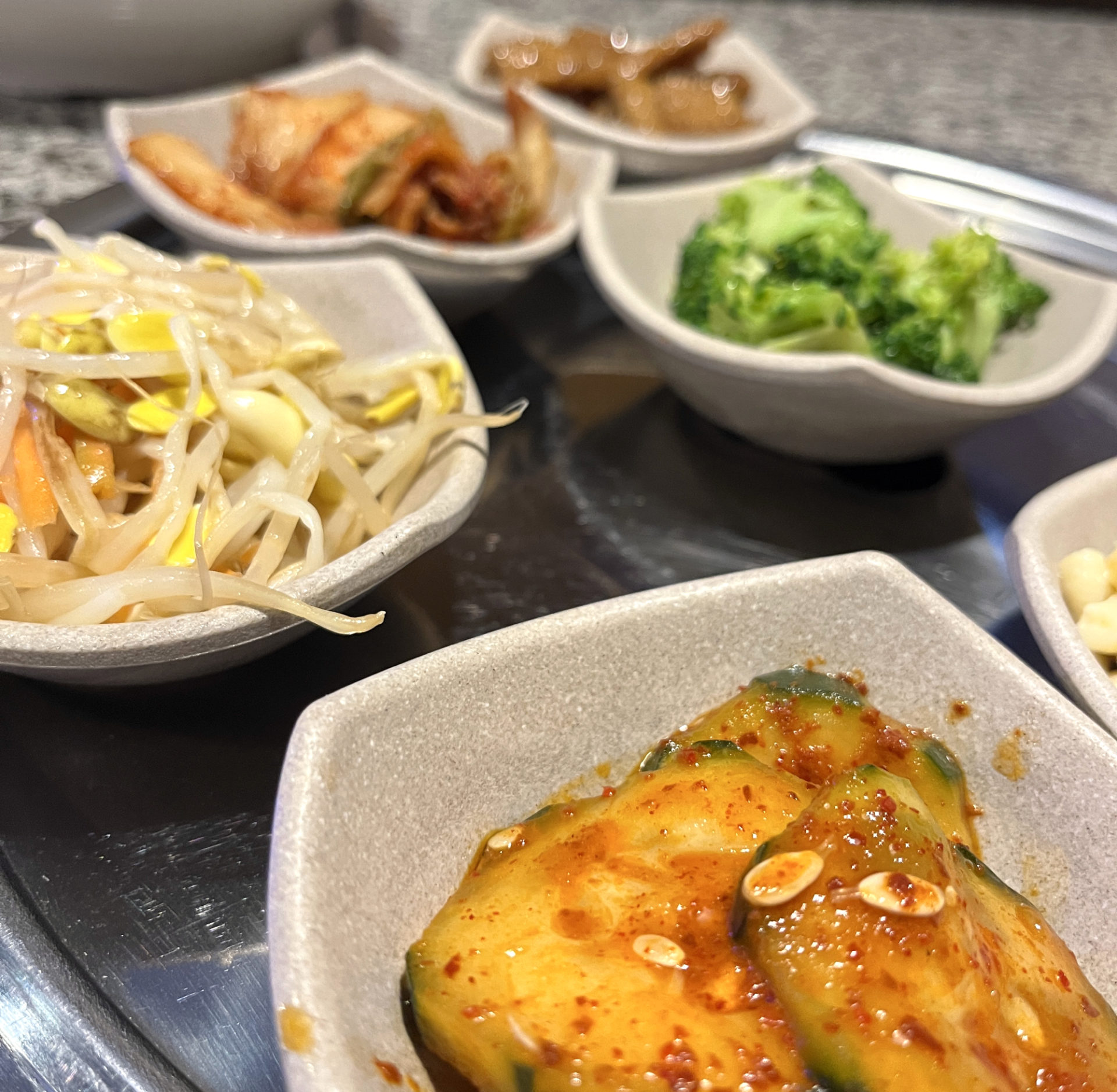 Banchan at Star BBQ: small bowls of side dishes including kimchi cucumber, pickled sprouts, kimchi, broccoli salad, and fish cakes.