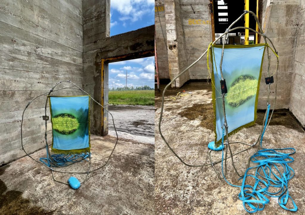 a two picture collage of "feral" by Melissa Pokorny. The images show the front and back of a sculpture that is a fabric turquoise rectangle with lime green in the center. It is held up by a thin round wire enricling the rectangle. The sculpture is an abandoned building with fields visible through an open doorway. 