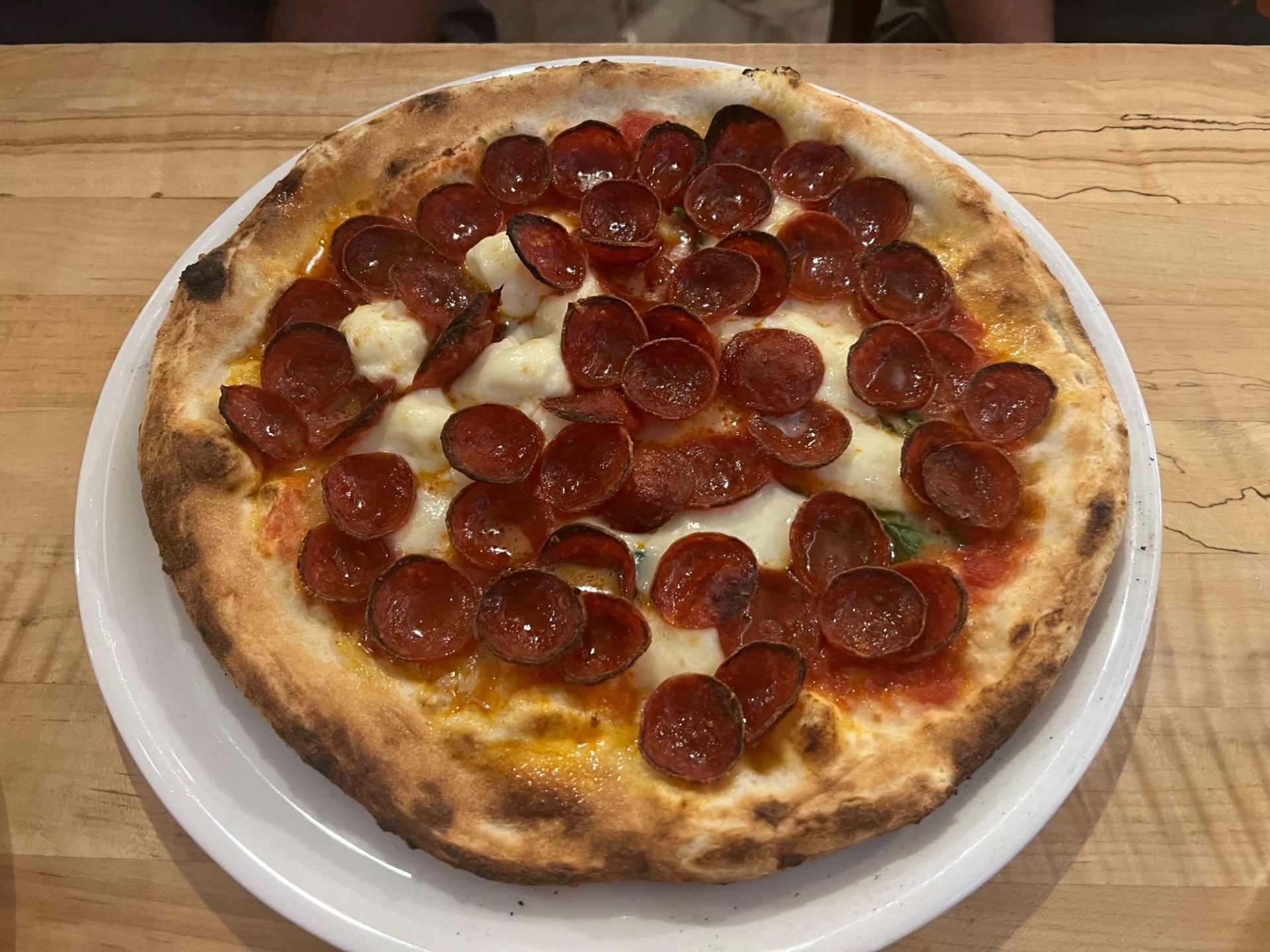 A round wood fired pizza covered in pepperoni.