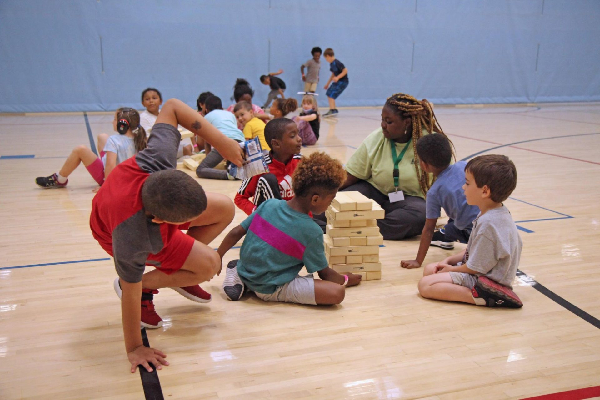 A group of kids are gathered with their camp leader, playing a stacking game.