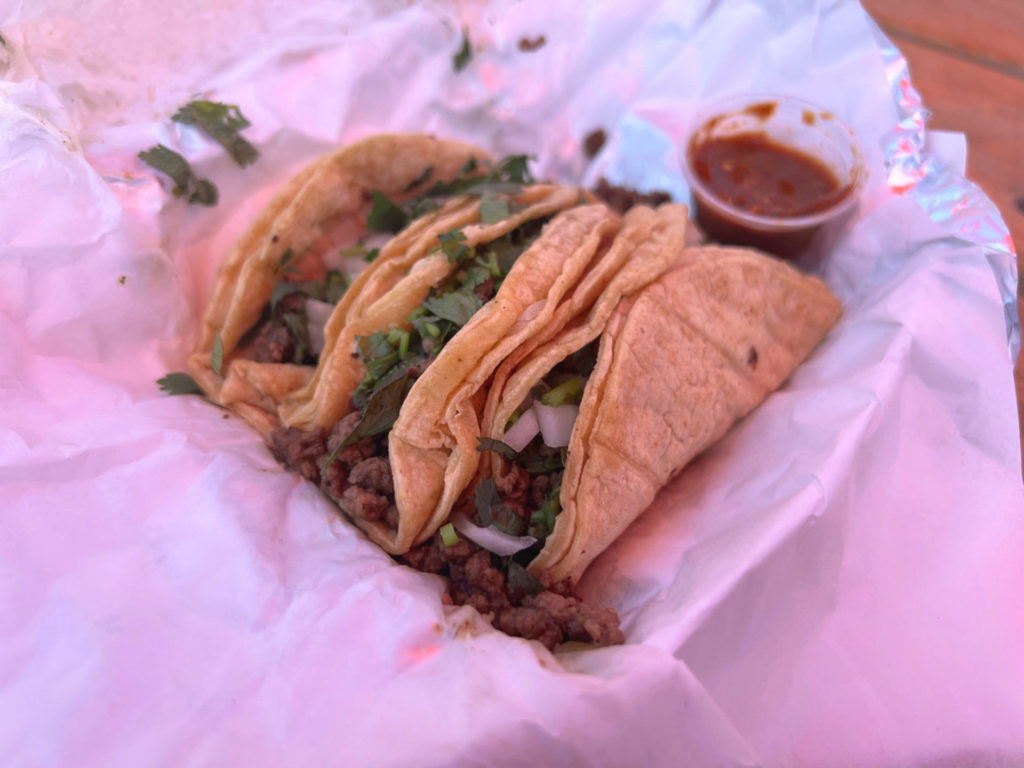Three ground beef tacos from Los Paisas taco truck has a small cup of red salsa. Photo by Alyssa Buckley.